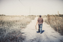 man walking down a dirt road with a suitcase 