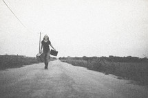 woman walking down a road carrying suitcases