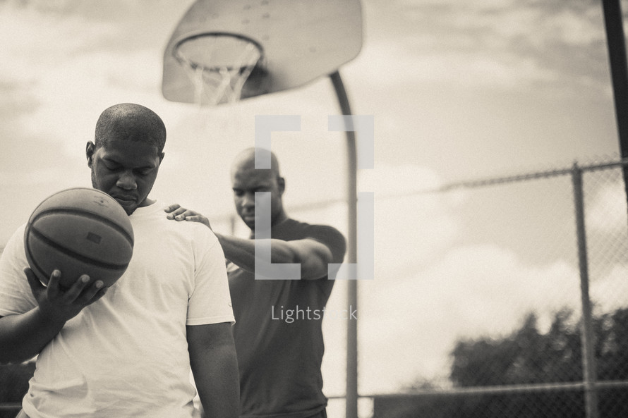 Men in prayer on a basketball court holding a basketball.