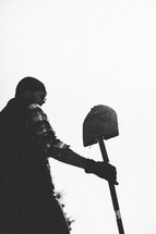 A man under a gray sky holds a shovel.