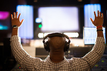 a man working a sound board with hands raised and a head set on 