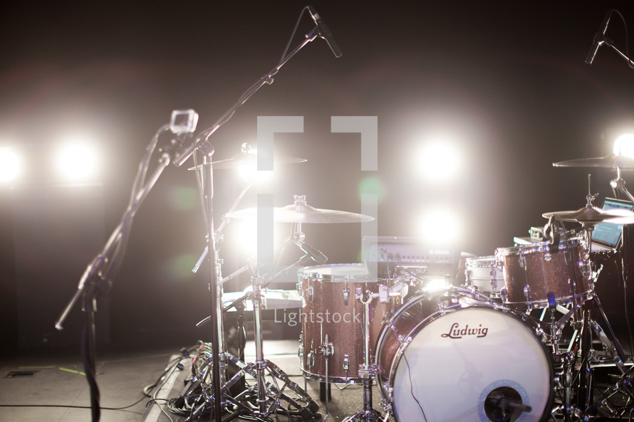 Stage lights shine on a drum set and microphones.