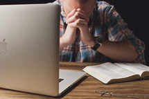 Praying with an open Bible, cross pendant, and a laptop computer.