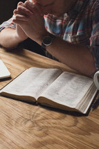 Man praying over a Bible at a wooden table.
