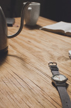 Coffee cup and urn on a wooden table with a wrist watch and the Bible.