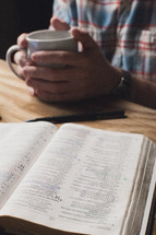 man holding a cup of coffee reading a Bible 