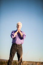 a man standing outdoors with praying hands 