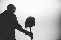 A man stands under a gray sky holding a shovel.