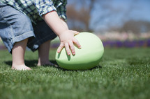 Child reaching down for a giant Easter egg in the grass.