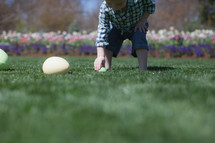 Young boy picking up an Easter egg in a flower garden
