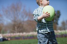 Young boy holding a oversized Easter egg in a flower garden