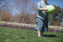 Young boy holding an oversized Easter egg, in a flower garden