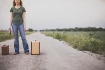 woman standing in the middle of a road next to suitcases