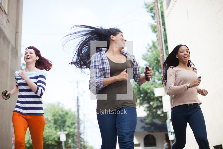 teen girls running down a street carrying cellphones 