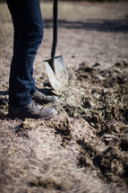 A man in jeans and boots digs with a shovel in the dirt.