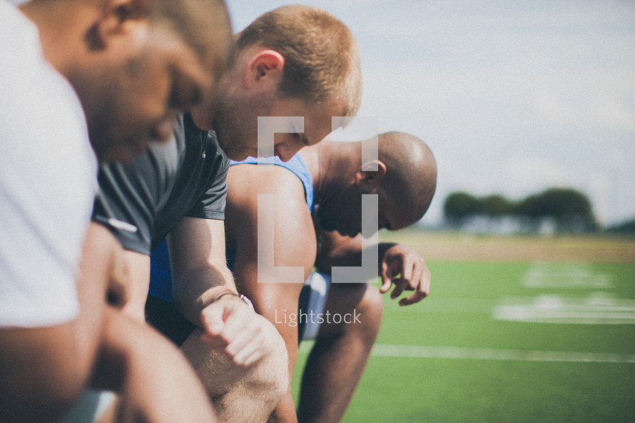 men in prayer on a football field 