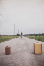 woman running down a long road towards two suitcases