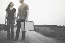 man and woman standing in the middle of a road carrying suitcases