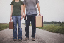 Couple with suitcases and a Bible standing in the middle of a dirt road.