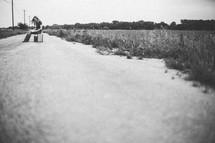 Woman sitting on a suitcase in the middle of a dirt road reading a bible.