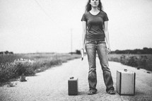 woman standing in the middle of a road next to luggage holding a Bible