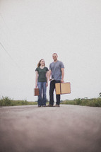 man and woman standing in the middle of a road carrying luggage
