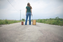 woman standing in the middle of a road next to suitcases