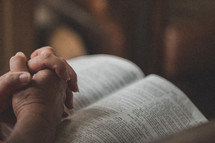Praying hands on an open Bible.