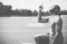 athlete in prayer on a football field pointing up to God