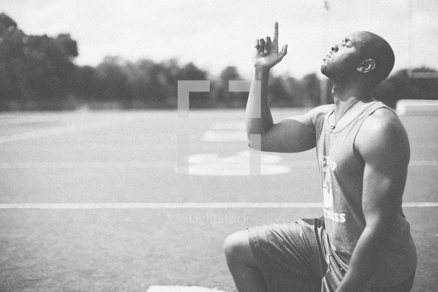 athlete in prayer on a football field pointing up to God