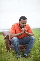 African-Amrican man sitting in a chair in a field with praying hands 