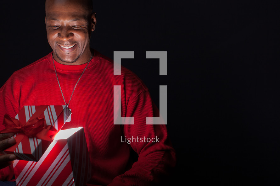 African American man looking happily into a Christmas gift box full of light.