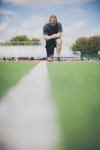 man kneeling in prayer on the football field 