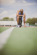 athlete kneeling in prayer on a football field 