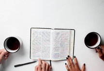 hands on pages of a Bible and coffee mugs 