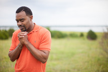 man standing outdoors in a field in prayer 