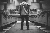 man looking down standing in the aisle of an empty church