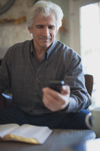 man looking at his cell phone with an open Bible 