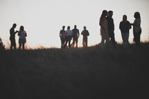 group gathered talking outdoors in a field at sunset 