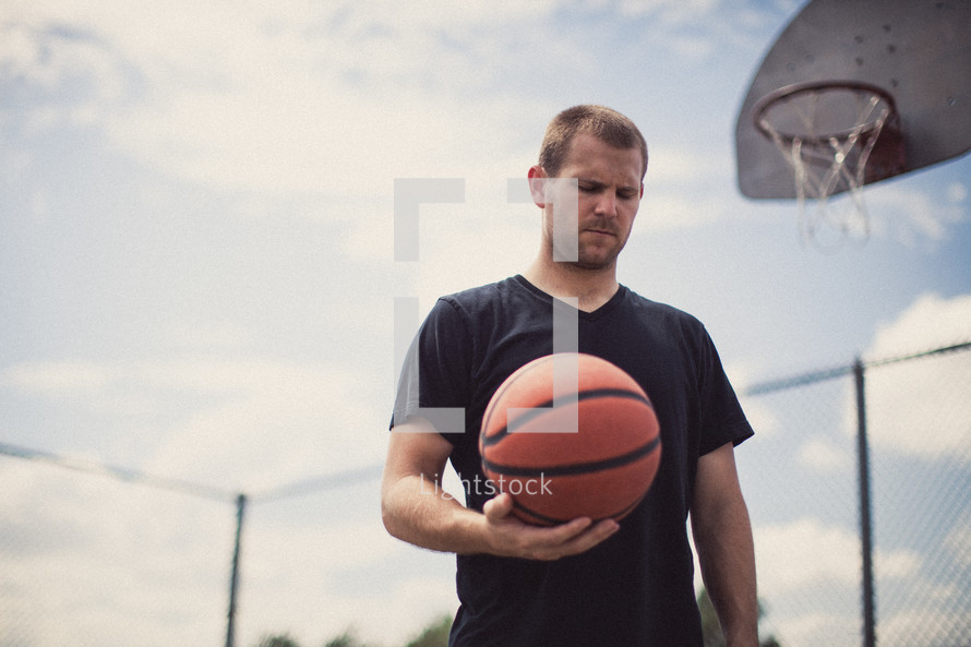 Man in prayer on a basketball court holding a basketball.