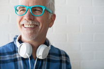 face of a man wearing reading glasses and headphones around his neck with a white beard 