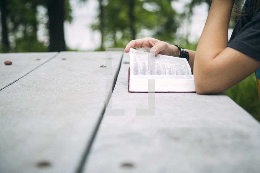 A woman sitting at a picnic table reading the Bible.