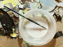 collage materials and paint brush in glue dish viewed from above