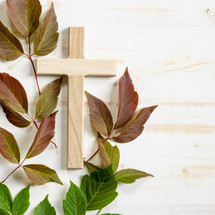 wooden cross with red and green leaves on a white wood background 