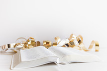 gold streamers and open bible on a white background