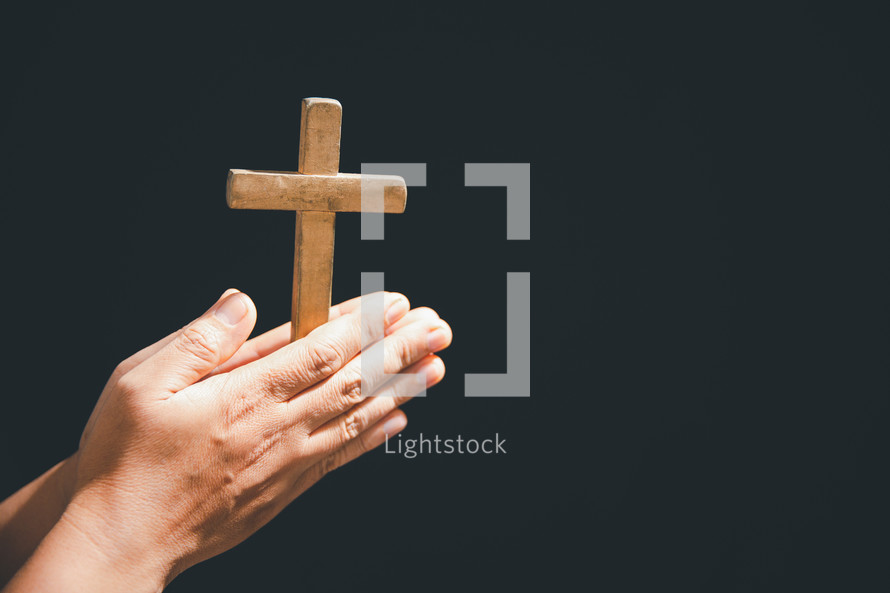Hands folded on a wooden cross