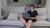 Focused male teenager playing game on laptop at home couch playing computer SPF or MMORPG game upset looking at screen focus on match disappointed lose defeated. 
