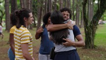 Beautiful people meeting and hugging each other at a park. Young friends enjoying time together. Happy guys and girls hugging while meeting outdoors.