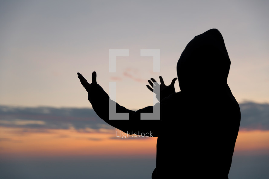 Silhouette of man in hood praying at sunset