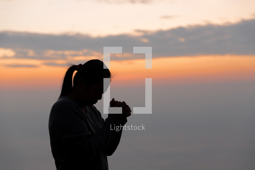 Silhouette of woman praying at sunset